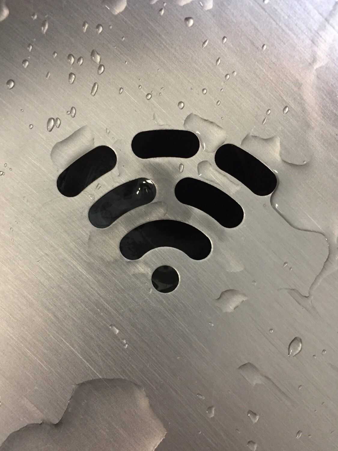Photo of a metal drain, where the drain grate looks like a wifi symbol with some water visible around the drain