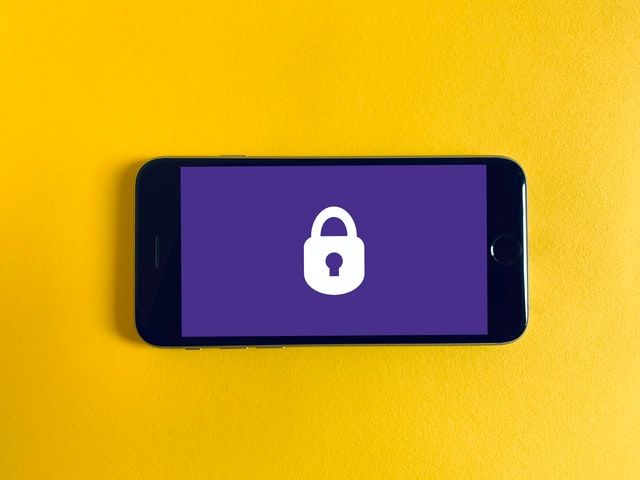 Image of a mobile phone on a yellow background. The phone has a purple display with a white locked security padlock in the centre. Image from Unsplash by  Franck
