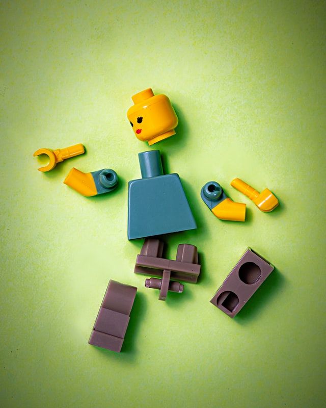 Green background and a Lego person in pieces. 