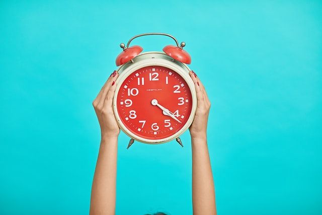 An orange clock held by two hands on a blue background. 