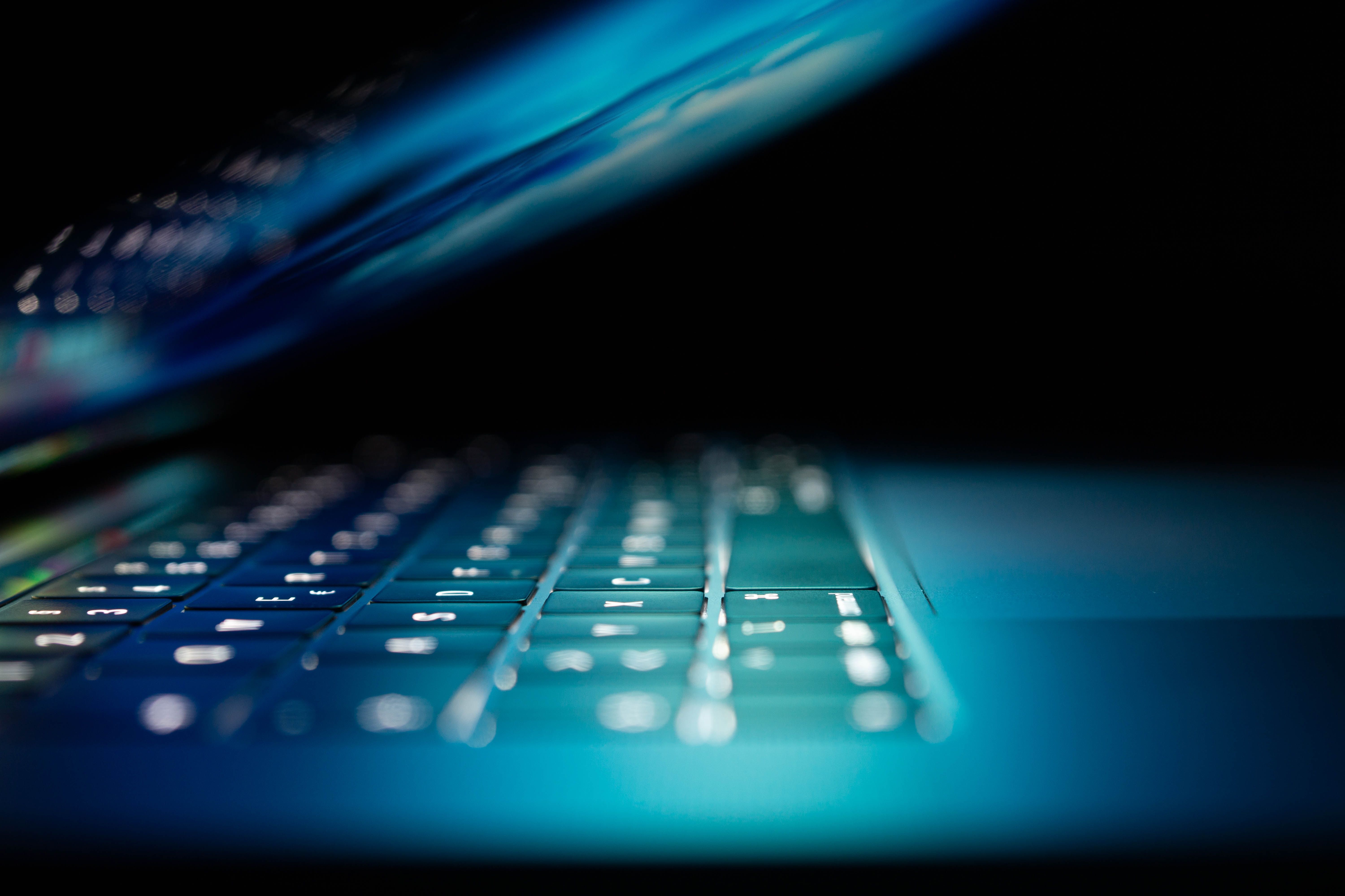 Image is of a laptop opened slightly, blue light glowing across the keyboard and touchpad.